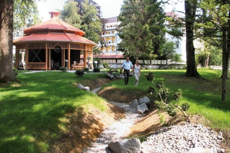 Ein ruhiger Spaziergang im Park mit Pavillon Zwei Personen spazieren vor einem Pavillon in einem grünen Park.