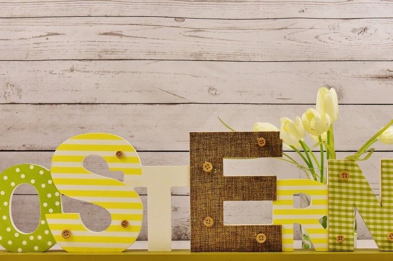 Osterdekoration mit Schriftzug und Tulpen Dekorativer Schriftzug 'OSTERN' in verschiedenen Materialien und Mustern, neben gelben Tulpen vor einer Holzwand.