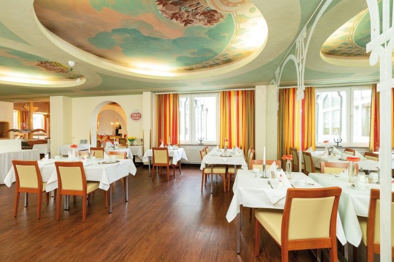 Stilvoll eingerichtetes Restaurant mit dekorativen Elementen Elegantes Restaurant mit hell dekoriertem Speisesaal, gedeckten Tischen und kunstvoll bemalter Decke.